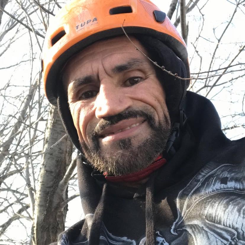 Hector wearing an orange safety helmet while working among trees